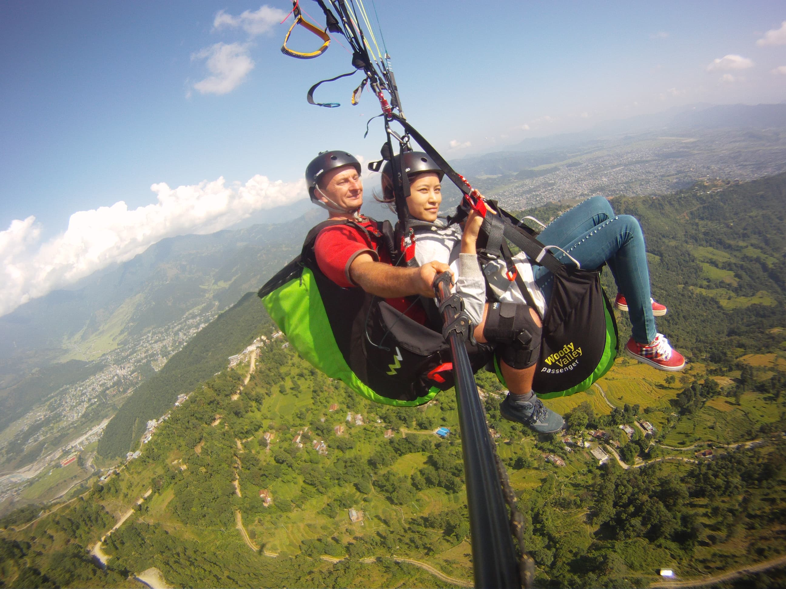 Two people paragliding above a green valley and mountain town